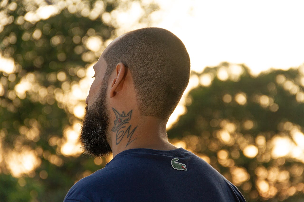 Silhouette of a bald, bearded man with a tattoo on his neck outdoors at sunset.