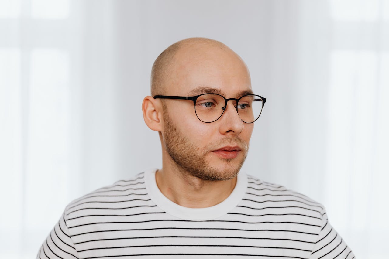 Portrait of a bald man with eyeglasses and a striped shirt looking away.