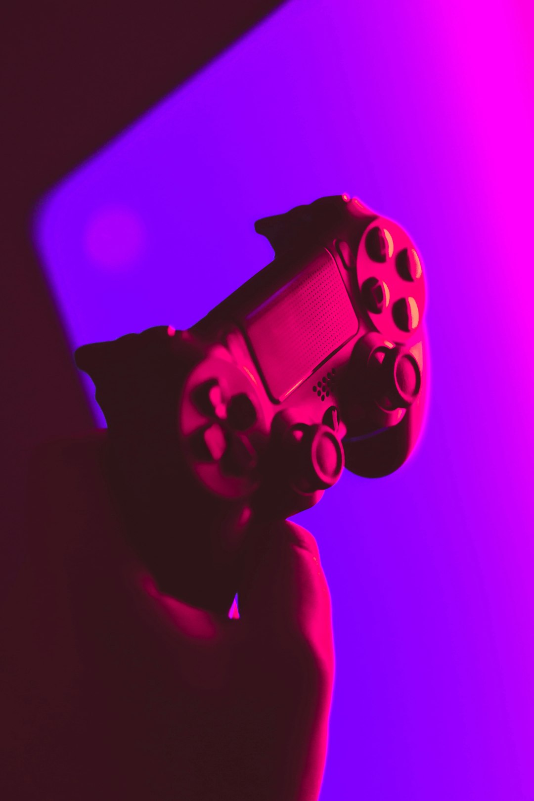 Pink neon colored video game controller on purple background